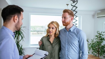 Ein Mann steht mit einem Klemmbrett mit Unterlagen vor einem Paar