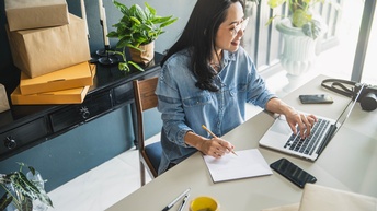 Person mit Brille sitzt an einem Schreibtisch und arbeitet mit einem Laptop
