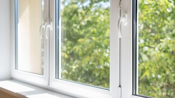 Nahaufnahme eines Fensterrahmens, der in drei Abschnitte eingeteilt. Hinter den Fenstern sind grüne Blätter