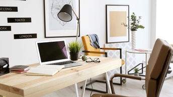 Gemütlicher Arbeitsplatz mit Schreibtisch, Laptop, Notizbücher, Brillen, Bürosessel und angenehmer und heller Arbeitsraumgestaltung