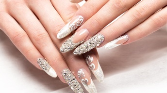 Nahaufnahme von langen Fingernägeln mit glitzernden Strasssteinen.