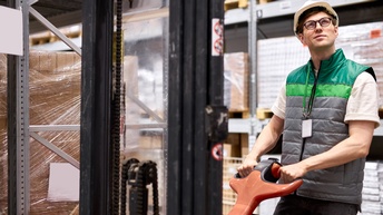 Person mit Schutzhelm und Blick nach oben betätigt Palettenheber in Lager