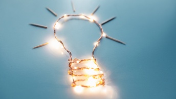 Eine Glühbirne, die aus Draht gebastelt ist auf blauem Hintergrund. Die Glühbirne leuchtet teilweise