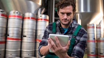 Person sitzt  in Lagerhalle und bedient Tablet, Getränkekartuschen im Hintergrund