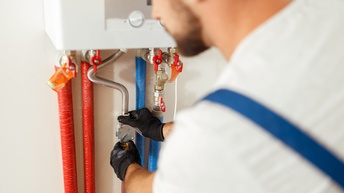 Nahaufnahme von einer Person, die eine Therme wartet und dabei Schutzkleidung trägt