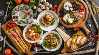 Verschiedene Pastagerichte, Käse, Prosciutto, Baguette, Tomaten, Champignons, Kräuter, Himbeeren, Brombeeren, Parmesan auf Tellern und Holzbrettern