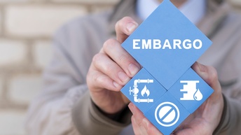 Nahaufnahme von vier Quadern, die schräg von den Händen einer Person in die Kamera gehalten werden. Auf dem obersten steht Embargo. Auf den Quadraten darunter sind Symbole wie ein Gashahn