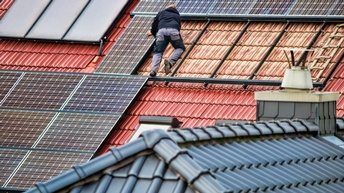 Person in Rückenansicht auf Dach gelehnt bei der Montage von Solarpanelen