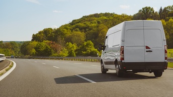 Weißer Transporter fährt auf einer Autobahn, inmitten einer grünen Landschaft