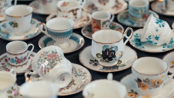 Nahaufnahme verschiedener weißer Tassen mit Blumenmustern und Untertassen mit Blumenmustern auf einem Tisch mit dunklem Tischtuch.