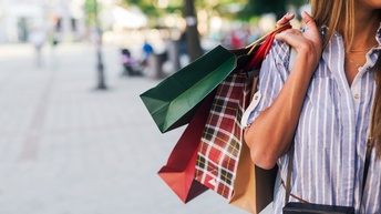 Detailansicht einer Person, die Einkaufstüten mit der Hand über die Schulter trägt