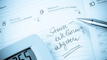 Eintrag in einem physischen Kalenderblatt mit Steuererklärung abgeben, daneben liegt ein Kugelschreiber sowie ein Taschenrechner