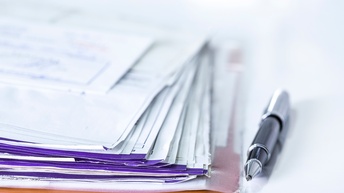 Detailansicht von aufeinander gestapelten Dokumenten, daneben Kugelschreiber liegend