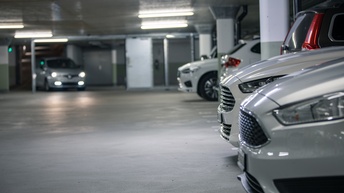 Autos stehen in einer Parkgarage, ein Auto fährt mit eingeschalteten Lichtern
