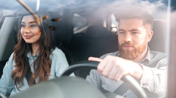 Zwei sanft lächelnde Personen in Auto sitzend, eine Person lenkend