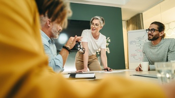 Personen mit Brillen unterhalten sich freudig und aufmerksam an einem Tisch in einem Besprechungsraum