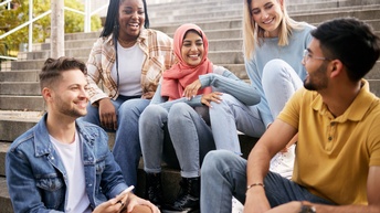 Jugendliche sitzen gemeinsam auf einer Treppe und unterhalten sich freudig miteinander
