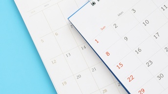 Nahaufnahme zweier übereinander, leicht versetz, liegender Ausschnitte von Kalenderblättern vor blauem Hintergrund