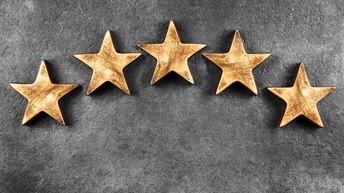 Fünf goldene Sterne liegen zu einem Halbkreis drapiert auf einem grauen Untergrund