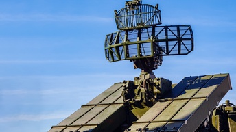 Auf einem großen, schweren, grünen Fahrzeug ist eine rechteckige Antenne befestigt. Im Hintergrund ist ein blauer Himmel mit ein paar Wolken