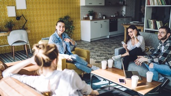 Gruppe junger Personen in buntgemustertem Raum auf Couchmöbeln sitzend unterhält sich und lacht