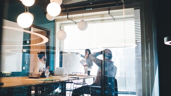 Drei Personen arbeiten mit Whiteboard und Dokumenten in modernem Konferenzraum