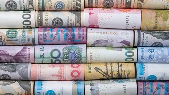 Nahaufnahme mehrerer, nebeneinander liegender, eingerollter Geldscheine in verschiedenen Währungen, zum Beispiel Dollar