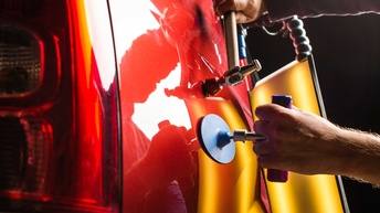 Ein Dellentechniker beim Ausbeulen einer Delle in einer Autokarosserie 