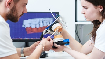 Zwei Personen bei Herstellung eines Zahnersatzes, Verwendung von zahntechnischen Apparaturen, Im Hintergrund Bildschirm mit Zahnsimulation