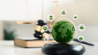 Weltkugel mit Grasoberfläche mit Overlay umgeben mit unterschiedlichen kreisrunden Symbolen zum Thema Nachhaltigkeit, im Hintergrund verschwommen Richterhammer, Buch und goldene Waage
