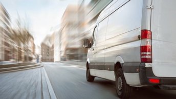 Weißer Transporter Rückansicht beim Fahren durch urbanes Gebiet, Umgebung in Bewegungsunschärfe