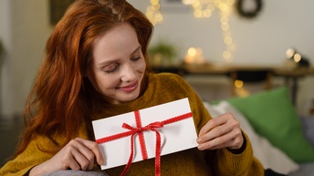 Eine Person hält mit beiden Händen ein weißes Kuvert, verziert mit einer roten Schleife