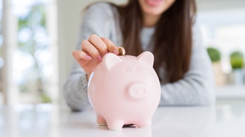 Close-up von einem rosa Sparschwein welches gerade mit einer Euromünze gefüttert wird