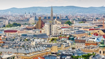 Panoramaaufnahme Teile der Stadt Wiens mit verschiedenen Sehenswürdigkeiten im Vordergrund. Im Hintergrund sind weitere Gebäude und Hügel