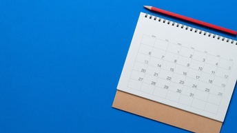 Auf blauem Untergrund liegt in der rechten Hälfte ein aufgeschlagenes Kalenderblatt. Darüber liegt ein Bleistift