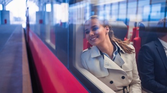 Außenansicht einer lächelnden Person, die am Fenster eines Zugwagons lehnt und hinausblickt
