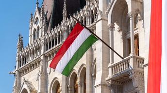 Die ungarische Flagge steckt in einem historischen Gebäude unter blauem Himmel.