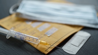 Nahaufnahme eines Impfpasses, einer Spritze, eines Pflasters und eines Mundschutzes