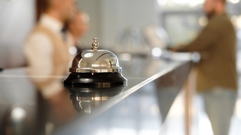 Analoge Rezeptionsklingel auf Tresen, im Hintergrund verschwommen Personen