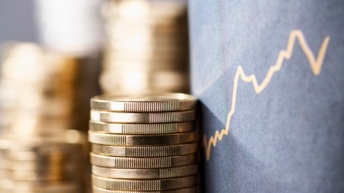 Vier Stapel Münzen sind neben einem grauen Display, auf dem ein Aktienkurs abgebildet ist