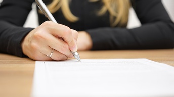 Eine Person unterschreibt mit einem Kugelschreiber auf einem bedruckten Blatt Papier