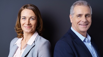 Portrait zweier sanft lächelnder Personen vor dunkelblauem Hintergrund
