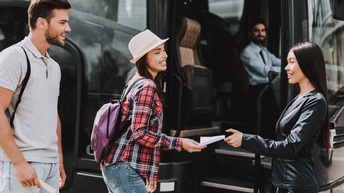 Zwei Personen stehen sich vor einer geöffneten Bustür gegenüber. Die linke Person übergibt der rechten Person einen Zettel. Hinter der linken Person steht eine weitere Person. Im Bus sitzt eine Person direkt hinter der Glasscheibe.