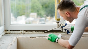 Person in Arbeitskleidung mit Schutzhandschuhen verarbeitet einen PU-Schaum bei einem Fensterrahmen