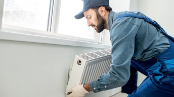 Person in blauer Arbeitskleidung bei der Montage eines Heizkörpers