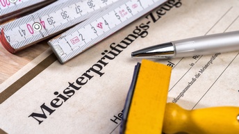 Detailansicht eines Meisterprüfungszeugnisses, daneben Zollstab liegend