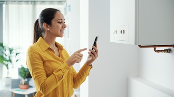Person steht vor Boiler und blickt lächelnd auf Smartphone, das sie in Händen hält