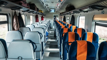 Leeres Zugabteil. Jacken hängen an Aufhängevorrichtungen. Koffer sind oberhalb der Sitze verstaut