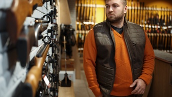 Zu sehen ist eine Person in einem Waffengeschäft. Sie betrachtet Schusswaffen und Gewehre, die in Nahaufnahme zu sehen sind.