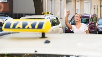 Person mit blonden geschlossenen Haaren hebt die Hand und ruft ein Taxi